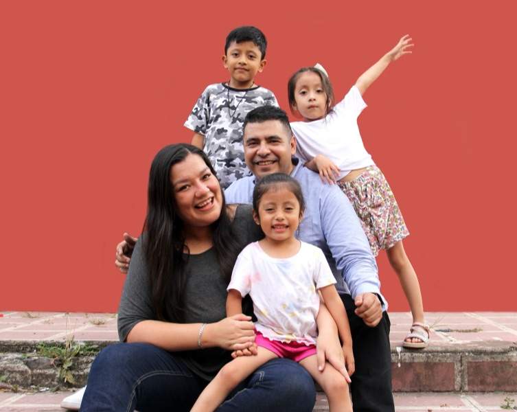 a happy hispanic family posed in front of a coral colored wall